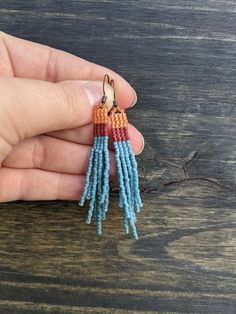 a hand holding a pair of small beaded tassels in blue and orange