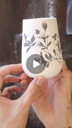 two hands holding up a white cup with flowers on the outside and grey circle at the top