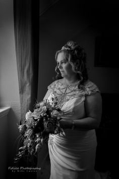 a woman in a wedding dress holding a bouquet and looking out the window at something