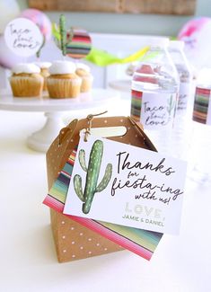 a table topped with cupcakes and cards on top of paper bags filled with water bottles