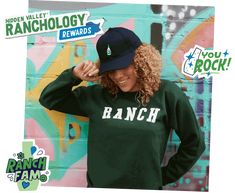 a woman in a green sweatshirt and hat standing next to a wall with stickers on it