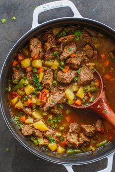 a pot filled with meat and vegetables on top of a table next to a wooden spoon