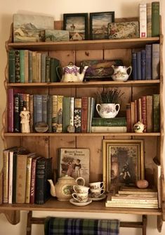 an old wooden shelf with books and tea cups on it, along with other antique items