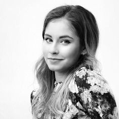 a black and white photo of a woman with long hair wearing a floral shirt looking at the camera