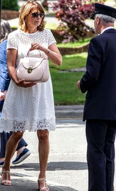 a woman in a white dress is holding a purse and talking to an older man