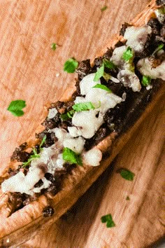 a wooden cutting board topped with a long piece of bread covered in meat and cheese