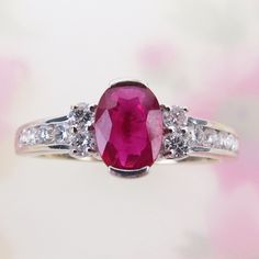 A vibrant natural ruby is centered on this attractive 14k white gold diamond ring. The .65 carat ruby is of deep raspberry pinkish-red color. It measures 6.5mm x 5mm x 2.5mm and is tightly held by two half-bezels.  Four bright and sparkly 2mm .03 carat diamonds flank the red gem. The shoulders are channel set with four 1.5mm diamonds (eight qty. with .12 carat total weight). Collectively, the ring has an estimated total weight of .25 carat or 1/4 carat. The inside is signed, "STS" (STS Jewelry Co., based in Austin, TX) and hallmarked "14k" (white gold). Please see detailed measurements below. The ring is in beautiful condition and would be lovely as an engagement ring or everyday statement ring. Wt: 2.5 grams US Ring size : 6.75 Length: 7.5mm or just over 1/4 Inch Width: 20mm or 13/16 Inch Lab-created Ruby Ring With Brilliant Cut In Oval Shape, Oval Diamond Ring With Lab-created Ruby Accents, Red Oval Sapphire Ring With Brilliant Cut, Red Oval Diamond Ring With Accents, Oval Lab-created Ruby Diamond Promise Ring, Oval Red Diamond Ring With Accents, Oval Ruby Ring With Diamond Accents For Promise, Red Oval Solitaire Diamond Ring, Oval Lab-created Ruby Diamond Ring In White Gold