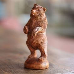 a small wooden bear figurine sitting on top of a wood table with blurry background