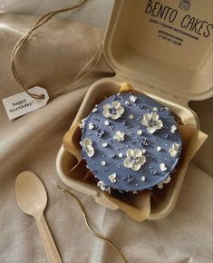 a blue cake in a box with spoons next to it on a tablecloth