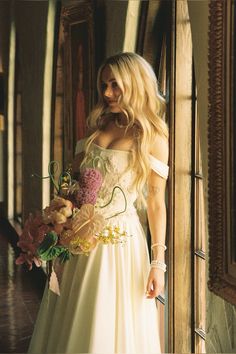 a woman in a white dress is holding a bouquet and looking at the camera while standing next to a doorway