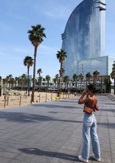 a woman standing in front of a tall building with palm trees on the sidewalk and talking on her cell phone