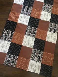 a black, white and brown patchwork quilt on a wooden floor