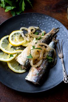 fish with onions and lemon slices on a black plate