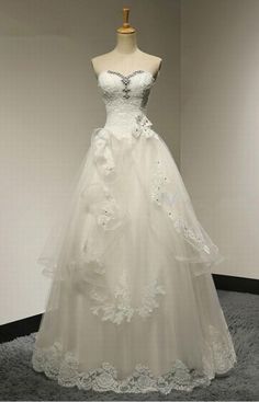 a white wedding dress on display in a room with gray carpet and wall behind it