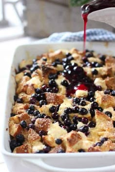 blueberry bread pudding being drizzled with red syrup from a spoon in a white casserole dish