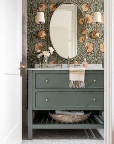 a bathroom with a green vanity and floral wallpaper on the walls, along with a round mirror