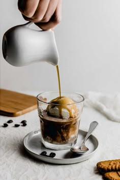 someone pouring ice cream into a glass with cookies on the table in front of them