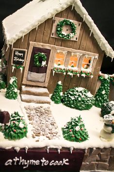 a gingerbread house decorated for christmas with snow on the roof and trees around it