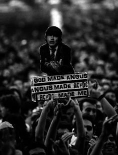 a man holding up a sign in the middle of a crowd with his hands raised