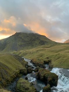 a river running through a lush green hillside next to a mountain covered in grass and rocks