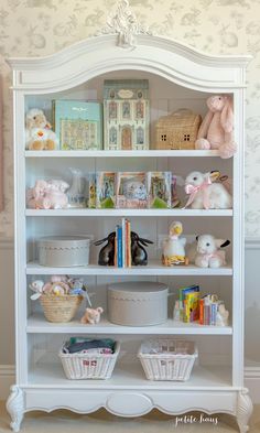 a white bookcase with stuffed animals and baskets on it's shelves in a child's room