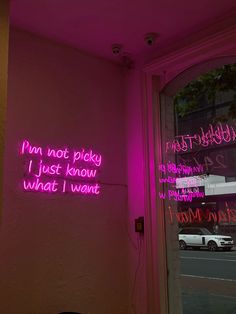 pink neon signs on the side of a building in front of a door and window