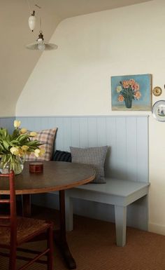 a dining room table and bench with flowers in vase on the back wall next to it