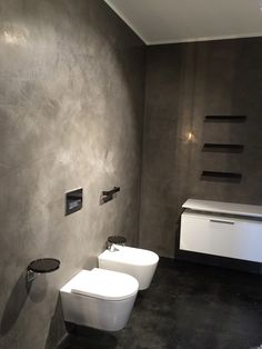 two white toilets sitting next to each other on a black floor in a gray bathroom