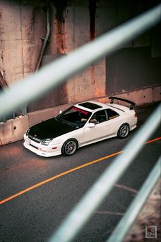 a white car parked on the side of a road next to a wall and fence