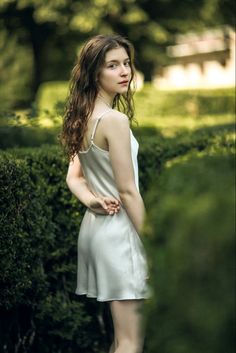 a woman standing in front of a hedge with her hands on her hips and looking off to the side