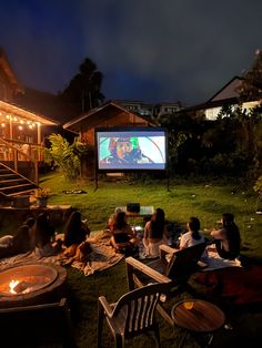 group of people sitting on the grass watching a movie in front of a house at night