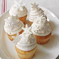 four cupcakes with white frosting and snowflakes on top are sitting on a plate