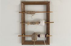 a wooden frame with yarn and scissors hanging from it's sides on the wall