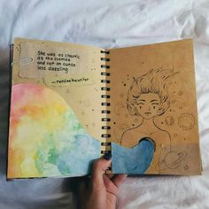 a hand holding an open notebook with a drawing on the cover and writing in it