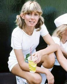 two women sitting next to each other holding drinks