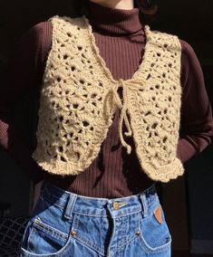 a woman is wearing a crocheted vest and denim shorts with her hands on her hips