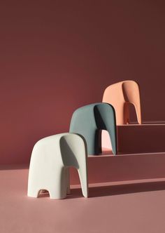 three different colored chairs sitting on top of a pink floor next to an elephant statue