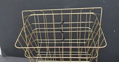 a gold wire basket sitting on top of a white table next to a black wall