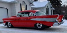 an old red car is parked in front of a house with snow on the ground