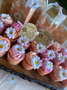 cupcakes with pink frosting and white flowers are on a wooden platter