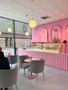 a woman sitting at a table in front of a pink wall with ice cream on it