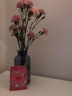 a vase filled with pink flowers sitting on top of a white table next to a card