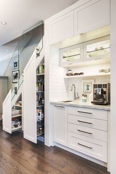 a kitchen with white cabinets and drawers under a stair case that leads to the second floor