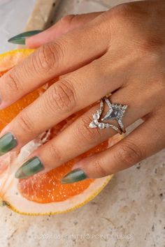 a woman's hand with green fingernails and ring on top of an orange slice