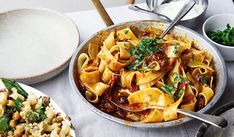 a pan filled with pasta and vegetables next to other dishes on a white table cloth