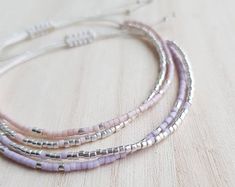 three bracelets with silver beads on a wooden surface, one is pink and the other is white