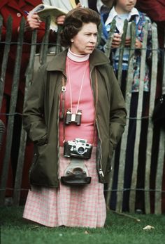 a woman standing in front of a fence with a camera on her shoulder and people behind her