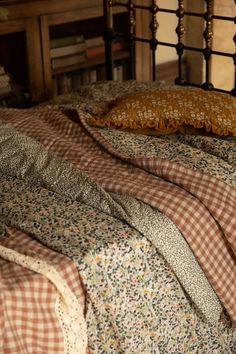 an unmade bed with plaid sheets and pillows on top of it, in front of a wooden headboard