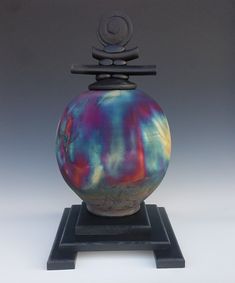 a colorful vase sitting on top of a wooden stand with a black base and metal handle