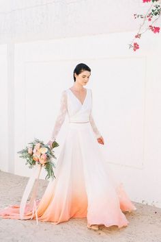 a woman in a white and pink wedding dress standing next to a wall with flowers on it